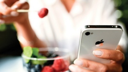 Woman eating fruits dessert with iPhone 4s in hands
