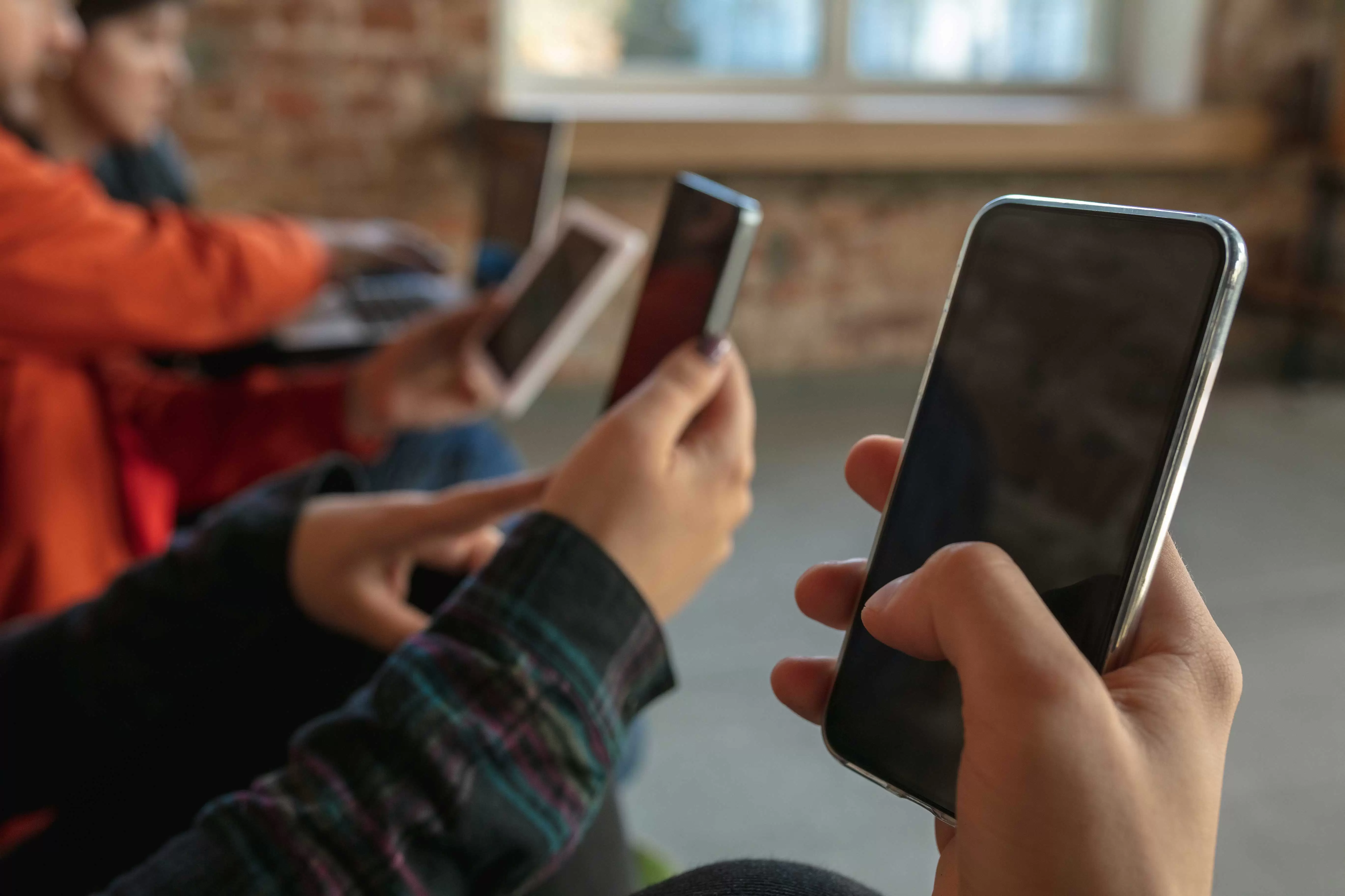 group happy young young people sitting sofa together sharing news photos videos from smartphones reading articles playing games having fun social media modern technologies